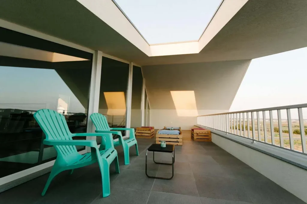 Guest house balcony with chairs, coffee table and two green plastic chairs.